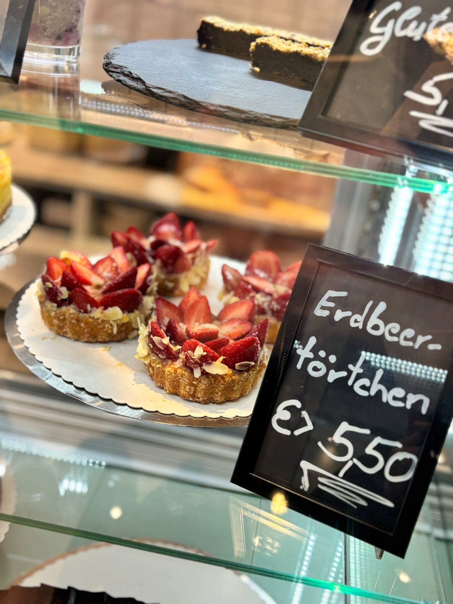 Frisches Erdbeertörtchen mit knusprigem Boden, Vanillecreme und glasierten Erdbeeren auf einem weißen Teller im Café Emilia in Essen.